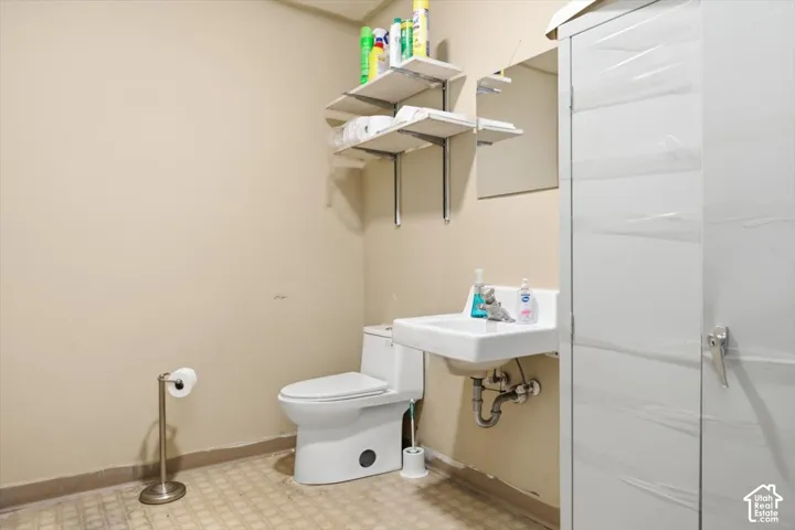 Wall-mounted sink with exposed plumbing, white toilet, and shelving units