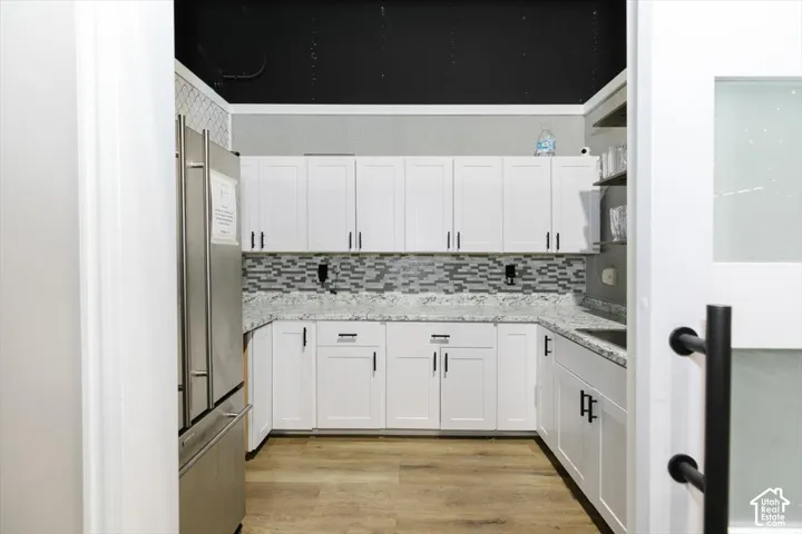 U-shaped kitchen featuring white cabinetry, gray and white mosaic tile backsplash, light wood-finish flooring, and a stainless steel refrigerator