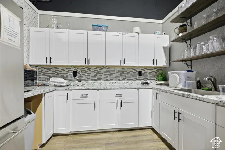 White shaker-style cabinetry with matte black hardware, mosaic tile backsplash, light-toned countertops, and wood-finish flooring