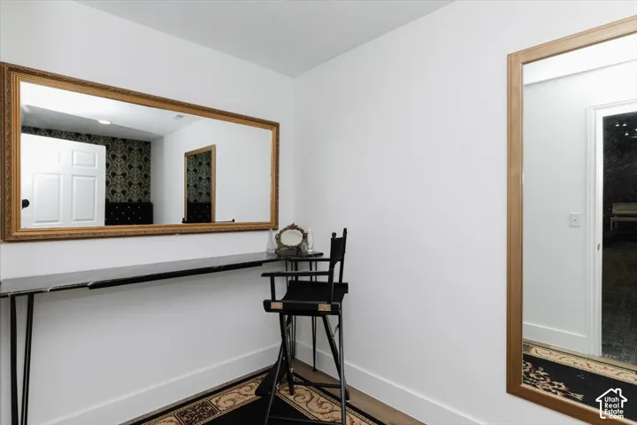 Wall-mounted mirror with an ornate gold-tone frame, black countertop, white walls, and wood-finish flooring