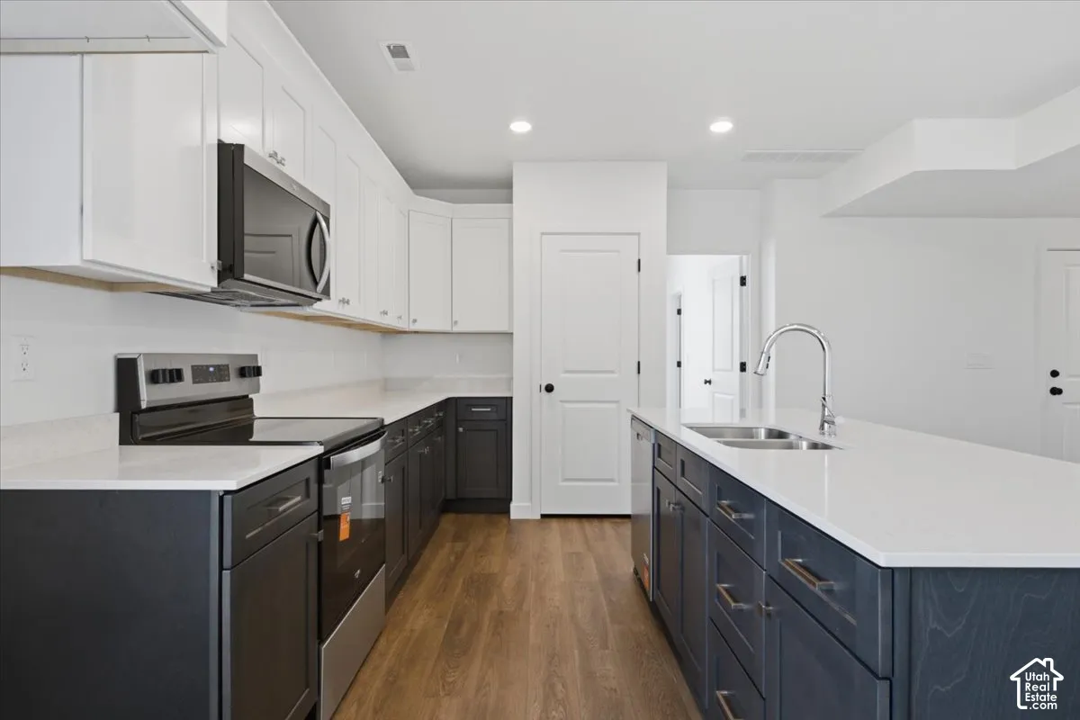 Kitchen featuring two-tone cabinetry, wood-finish flooring, white countertops, stainless steel appliances, and an island with an undermount sink