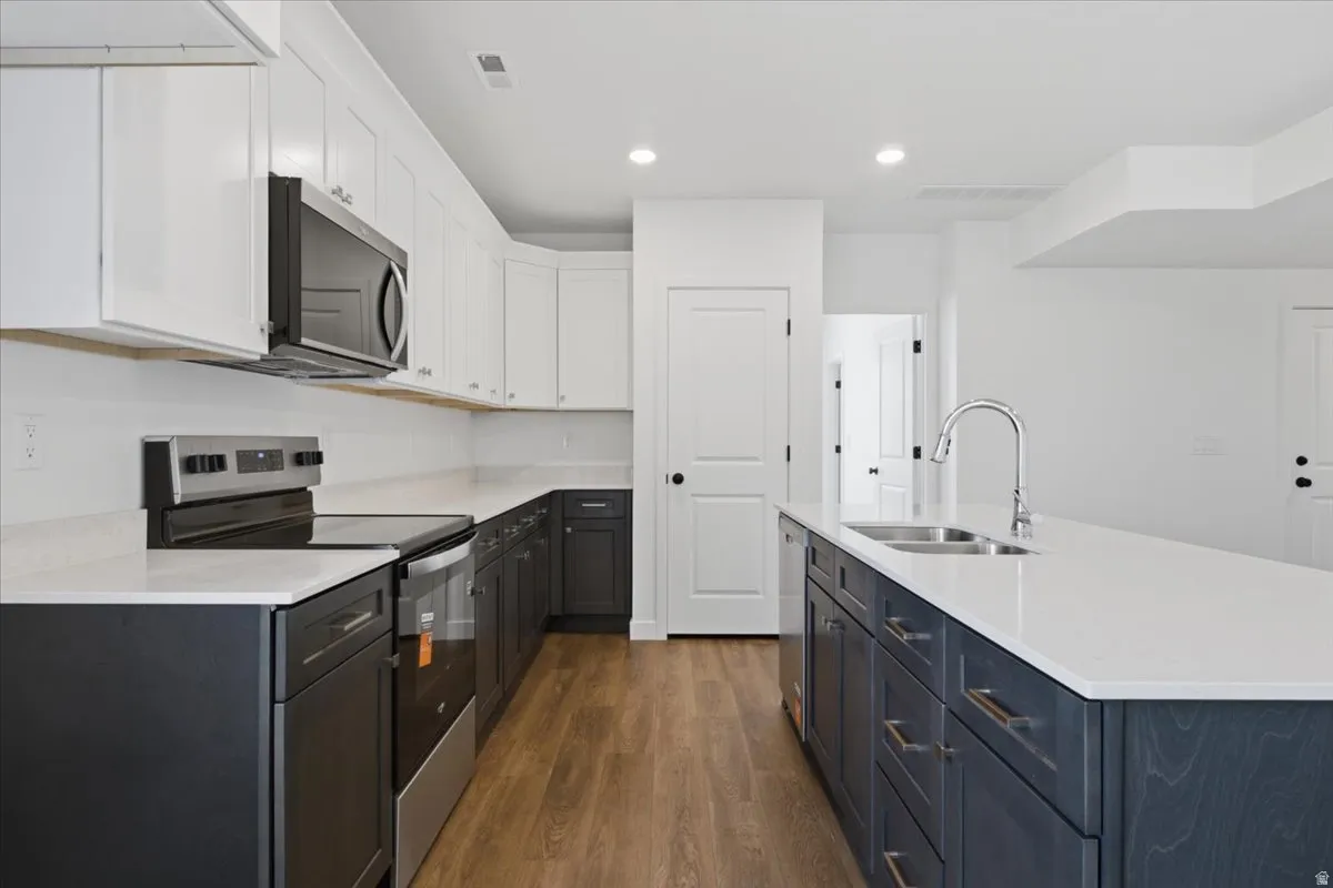 Kitchen featuring two-tone cabinetry, wood-finish flooring, white countertops, stainless steel appliances, and an island with an undermount sink