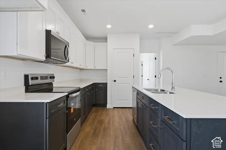 Kitchen featuring two-tone cabinetry, wood-finish flooring, white countertops, stainless steel appliances, and an island with an undermount sink