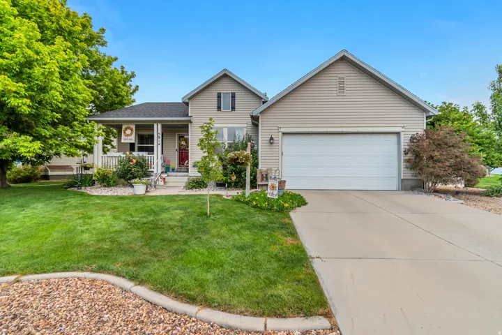 Siding exterior with a covered porch, attached garage, concrete driveway, and landscaped front yard with mature trees