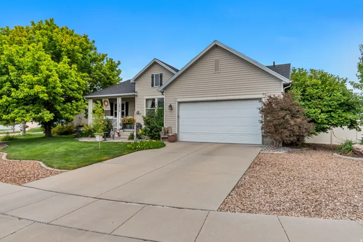 Two-story residence with light-colored siding, an attached garage, a covered front porch, a concrete driveway, and established landscaping