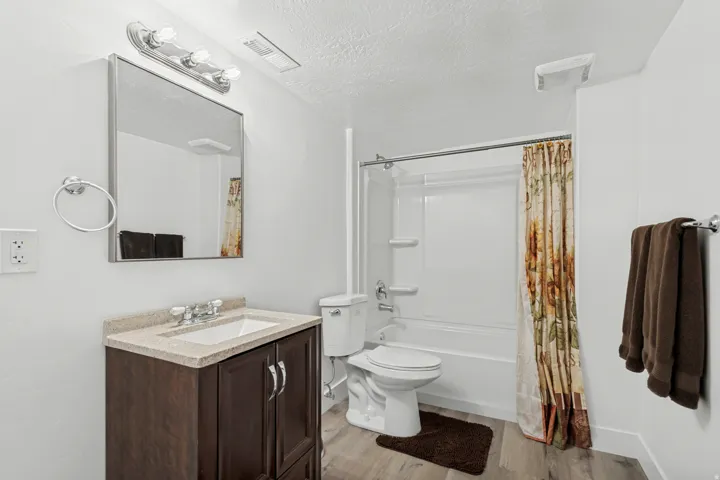 Bathroom featuring a wood-finish vanity with a light-toned countertop, a rectangular undermount sink, a chrome faucet, and a shower-over-tub combination with a white surround