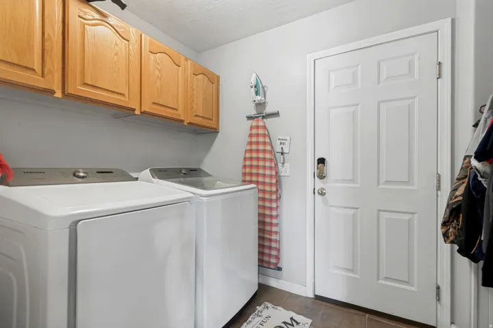 Laundry area featuring wood-finish cabinetry, a white paneled door, and durable tile flooring