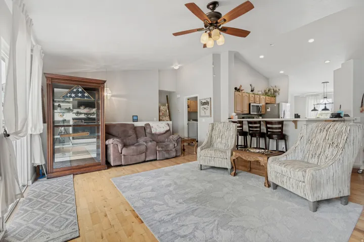 Vaulted ceiling with a ceiling fan, recessed lighting, wood-finish flooring, and a kitchen pass-through with counter seating