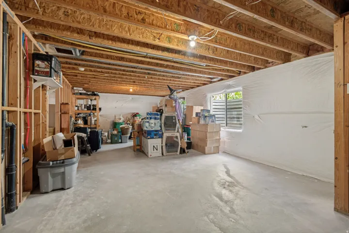 Unfinished basement featuring exposed wood joists, concrete flooring, and a window with a window well