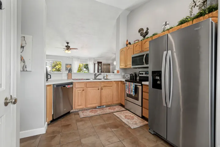 Kitchen with wood cabinetry, stainless steel appliances, white countertops, and tile flooring