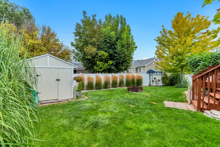 Expansive lawn featuring a storage shed, a fire pit, and a wooden deck with stairs