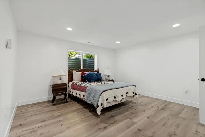 Recessed ceiling lighting, wood-finish flooring, white walls, and a window with a metal well