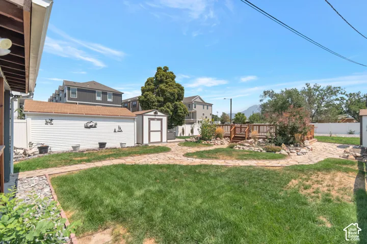 Expansive backyard featuring a manicured lawn, flagstone pathways, a wood deck, a storage shed, and a detached garage with horizontal siding