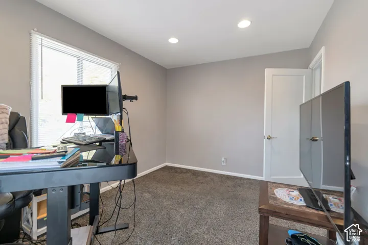 Spacious home office featuring recessed ceiling lighting, large windows with natural light, neutral wall finishes, and carpet flooring throughout