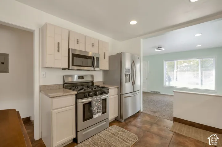 Stainless steel appliances, recessed lighting, tile flooring, light-colored cabinetry, and a large window