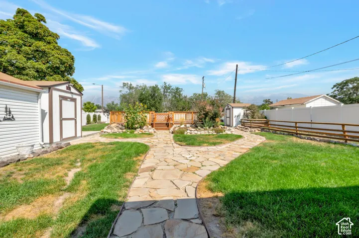 Walkway to the pool in the backyard featuring a natural stone pathway, manicured lawn, two storage sheds, and a wood deck