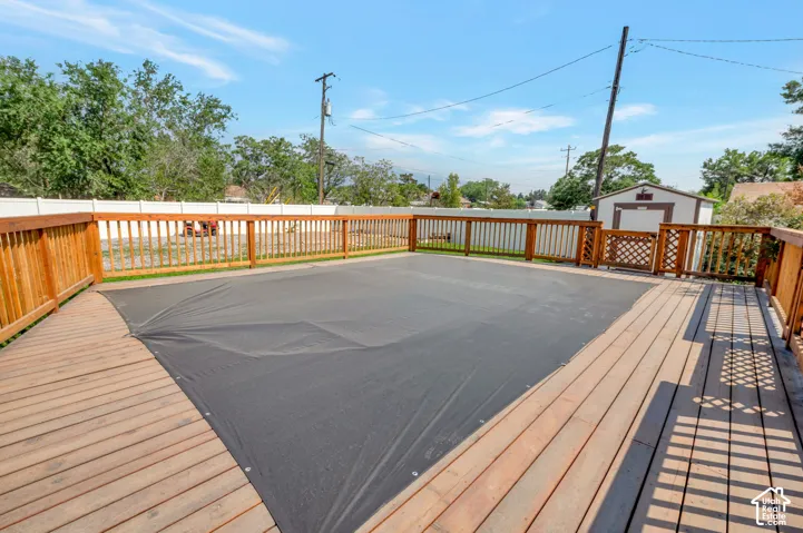 Expansive wooden deck surrounding a covered pool, featuring a perimeter wooden fence and an outdoor storage shed