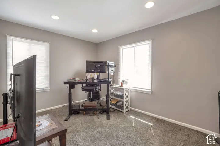 Recessed ceiling lighting illuminates a room with light gray wall paint and carpet flooring, featuring two windows with white blinds