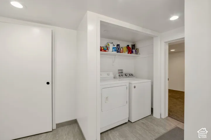 Across from the bathroom with easy access. Recessed lighting illuminates the laundry area featuring a white shelf and tiled flooring