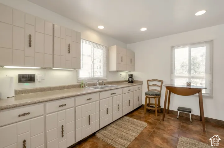 White cabinetry with decorative pulls, recessed ceiling lighting, a dual basin stainless steel sink, light-colored countertops, and tiled flooring