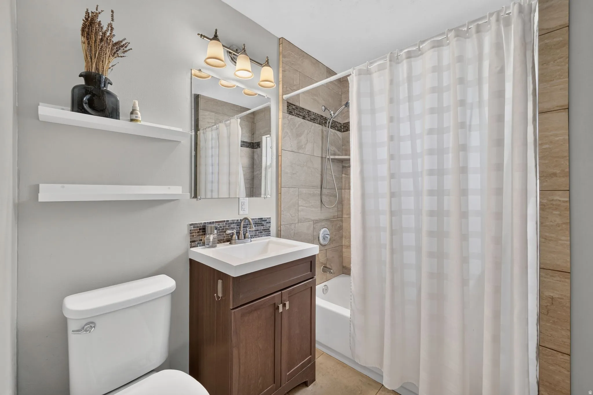 Built-in floating shelves, vanity with storage, tile backsplash, and a shower-over-tub combination with tiled walls