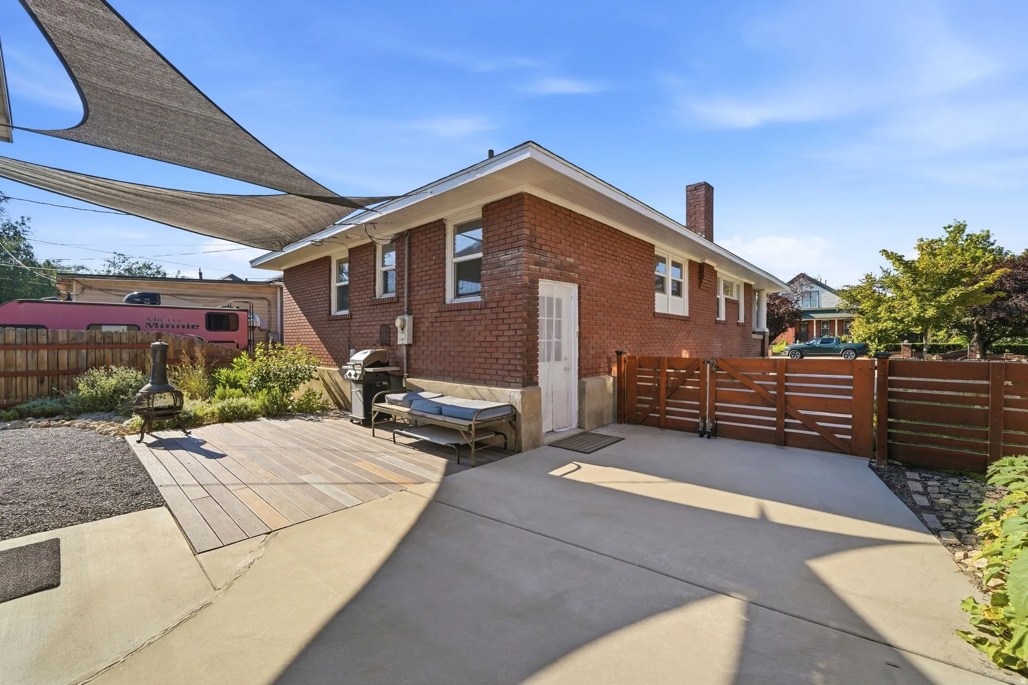 Brick exterior with a wood deck, concrete patio, and slatted wood fencing