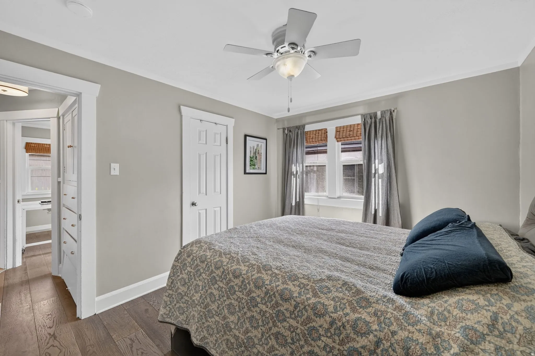 Wood-finish flooring, ceiling fan with light fixture, window with blinds and drapes, white paneled door, and built-in cabinetry