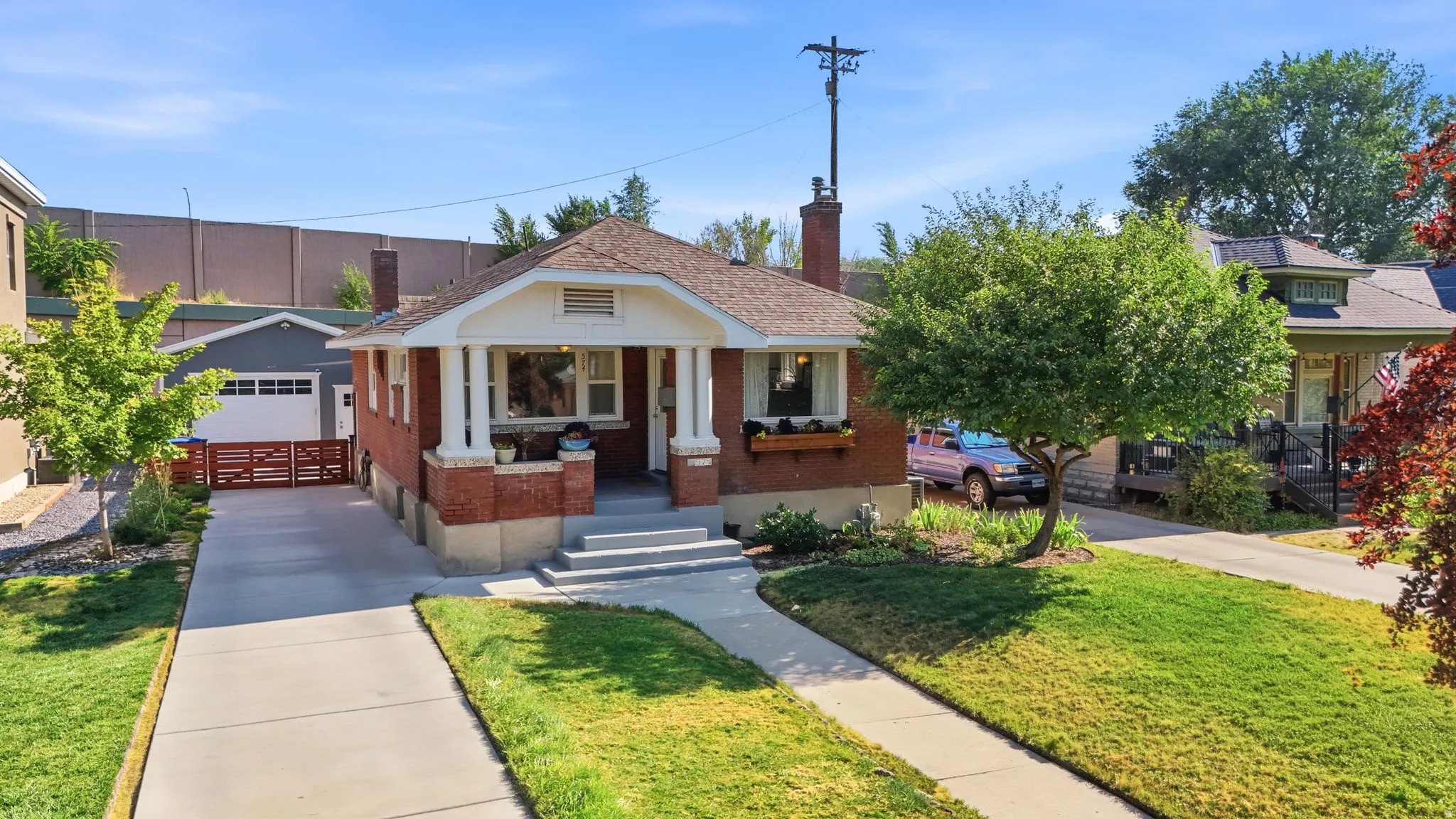 Brick exterior with a covered porch, established landscaping, detached garage, and paved driveway