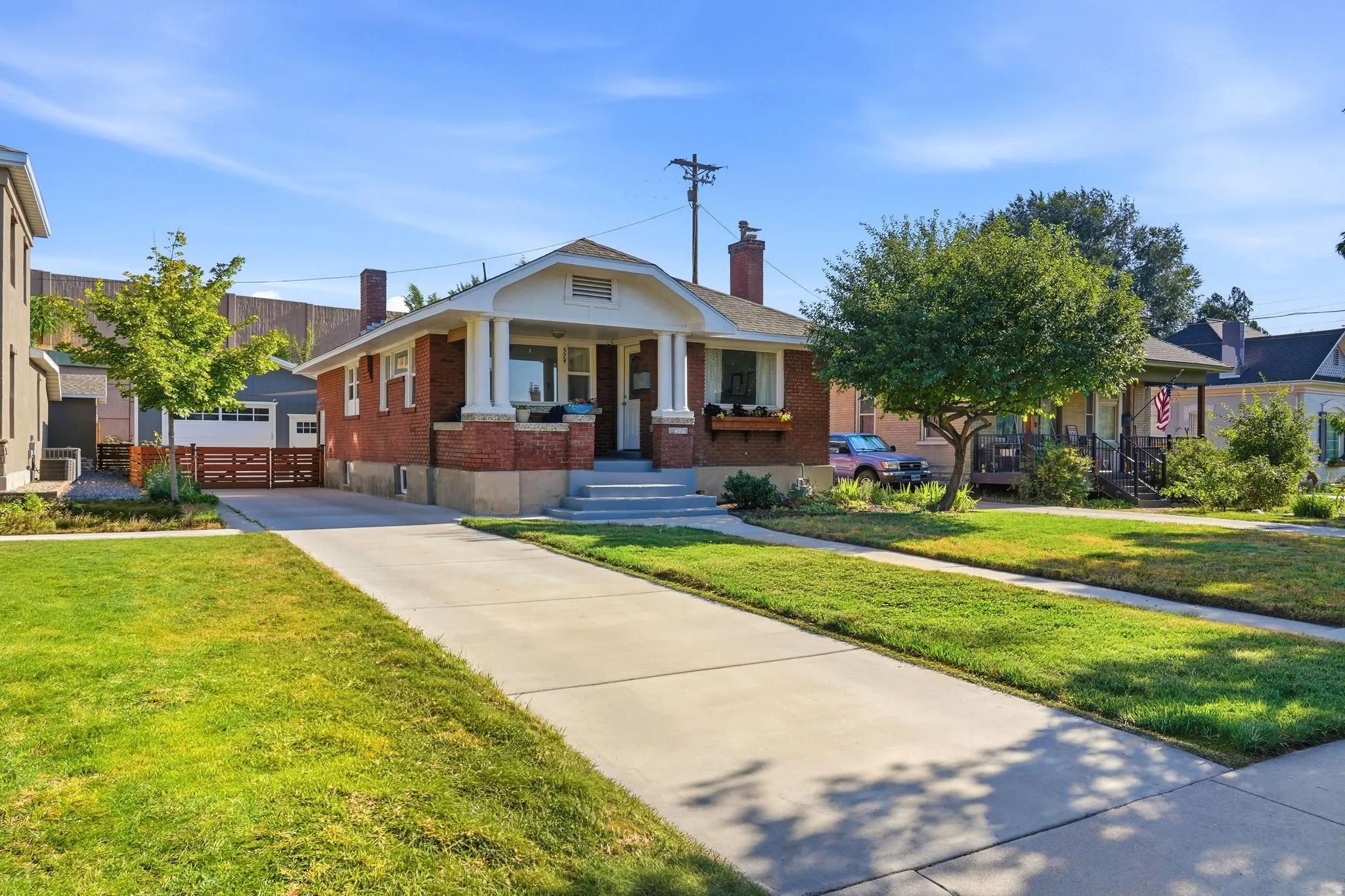 Brick exterior residence featuring a covered front porch, concrete driveway, manicured lawn, and detached garage