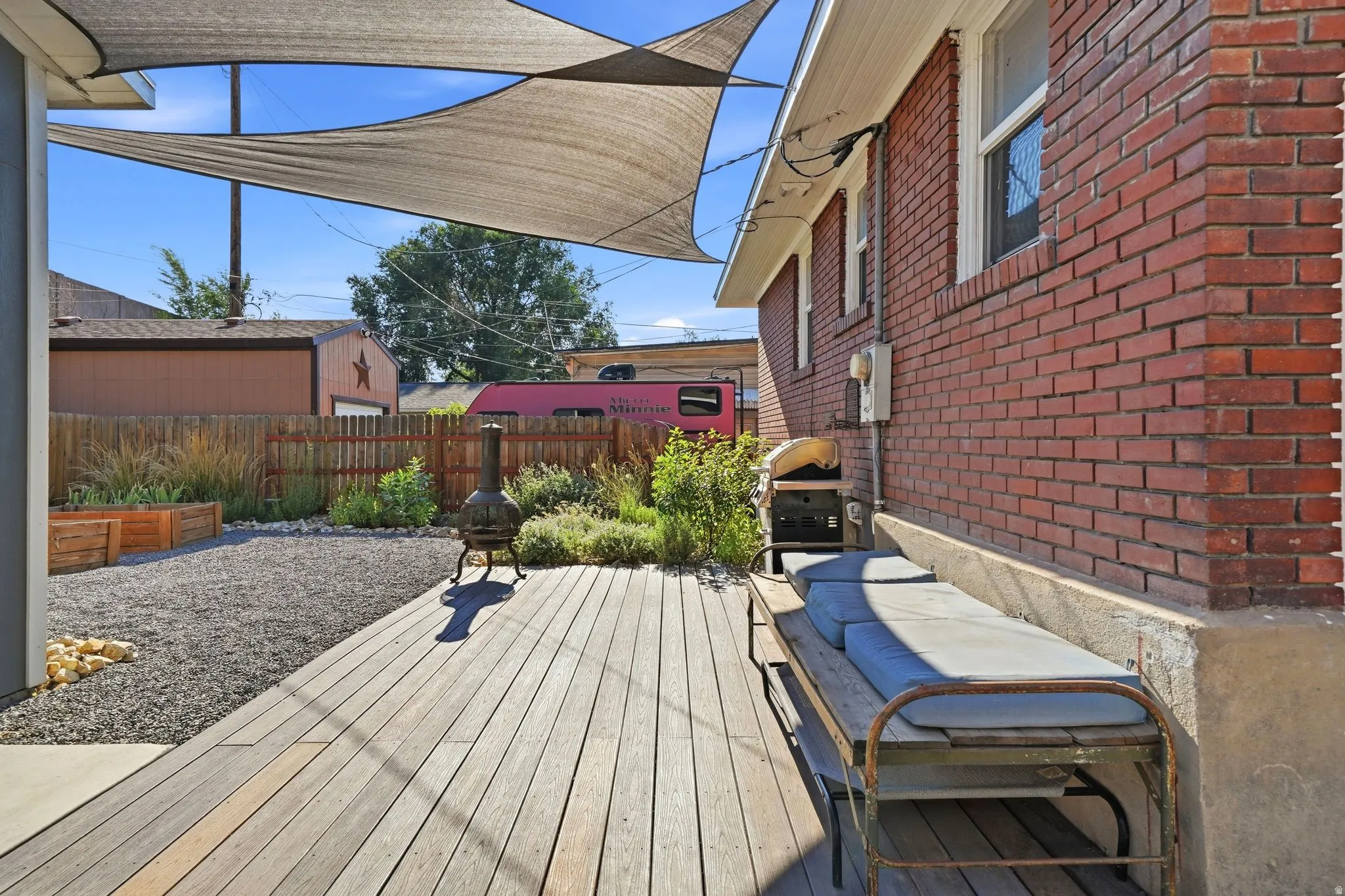Deck with horizontal wood planks, shade sails, and gravel landscaping with raised garden beds