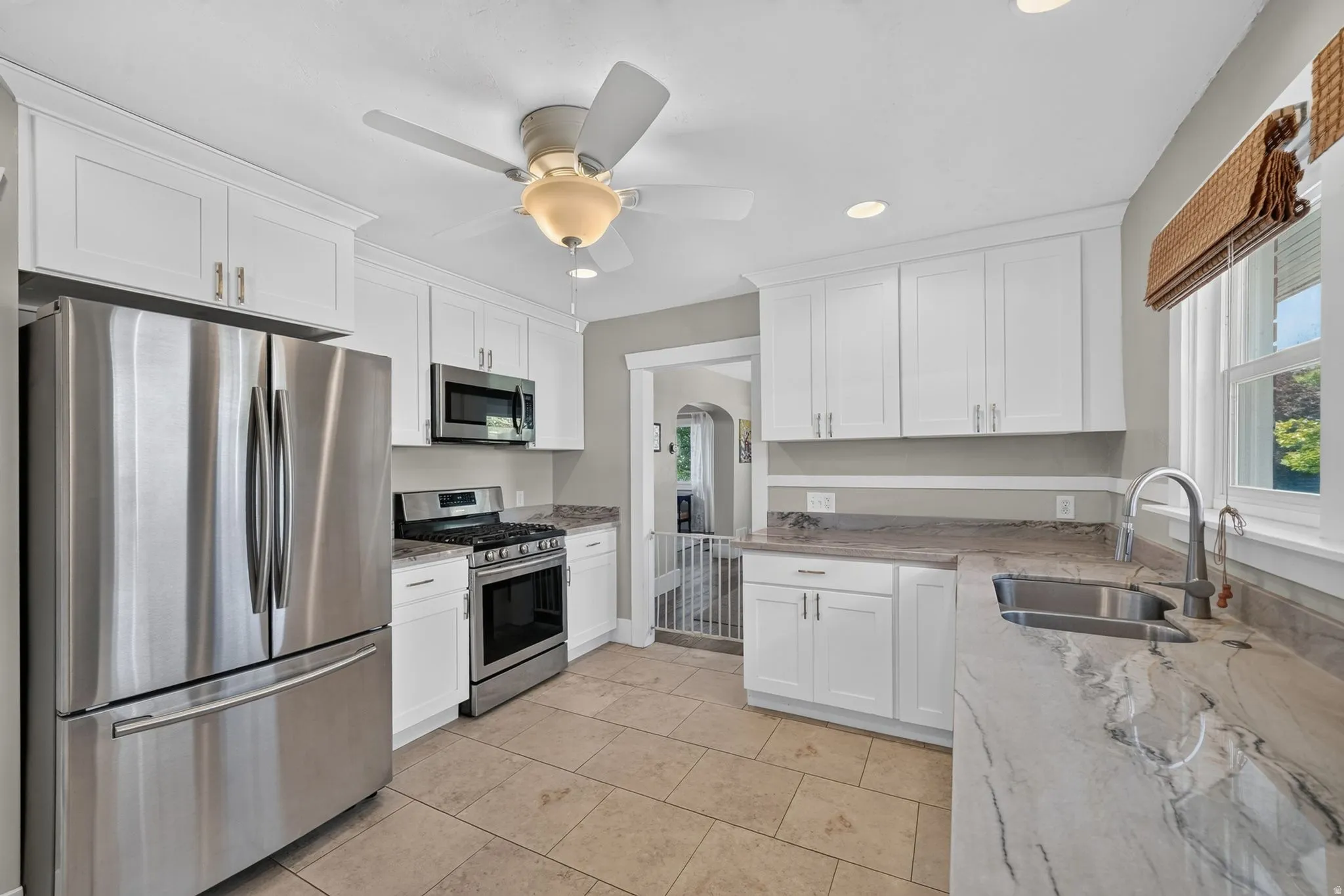White cabinetry with brushed nickel hardware, stainless steel appliances, dual basin sink, light-toned countertop, and tile flooring