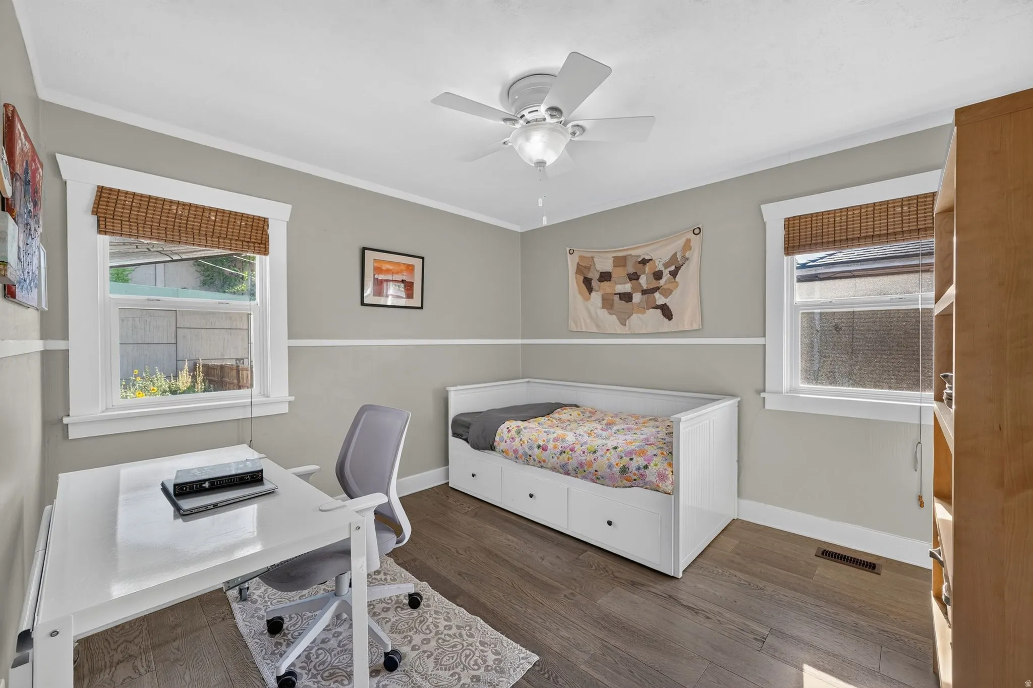 Hardwood-style flooring, white trim, ceiling fan with integrated lighting, and two windows with natural woven shades