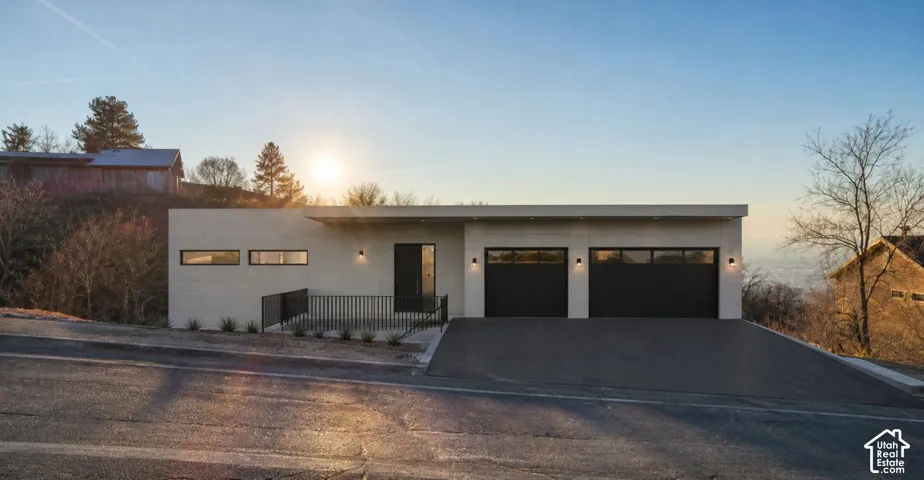 Modern exterior featuring a light-colored facade, a flat roofline, two contemporary garage doors with frosted glass panels, and a black metal railing entry