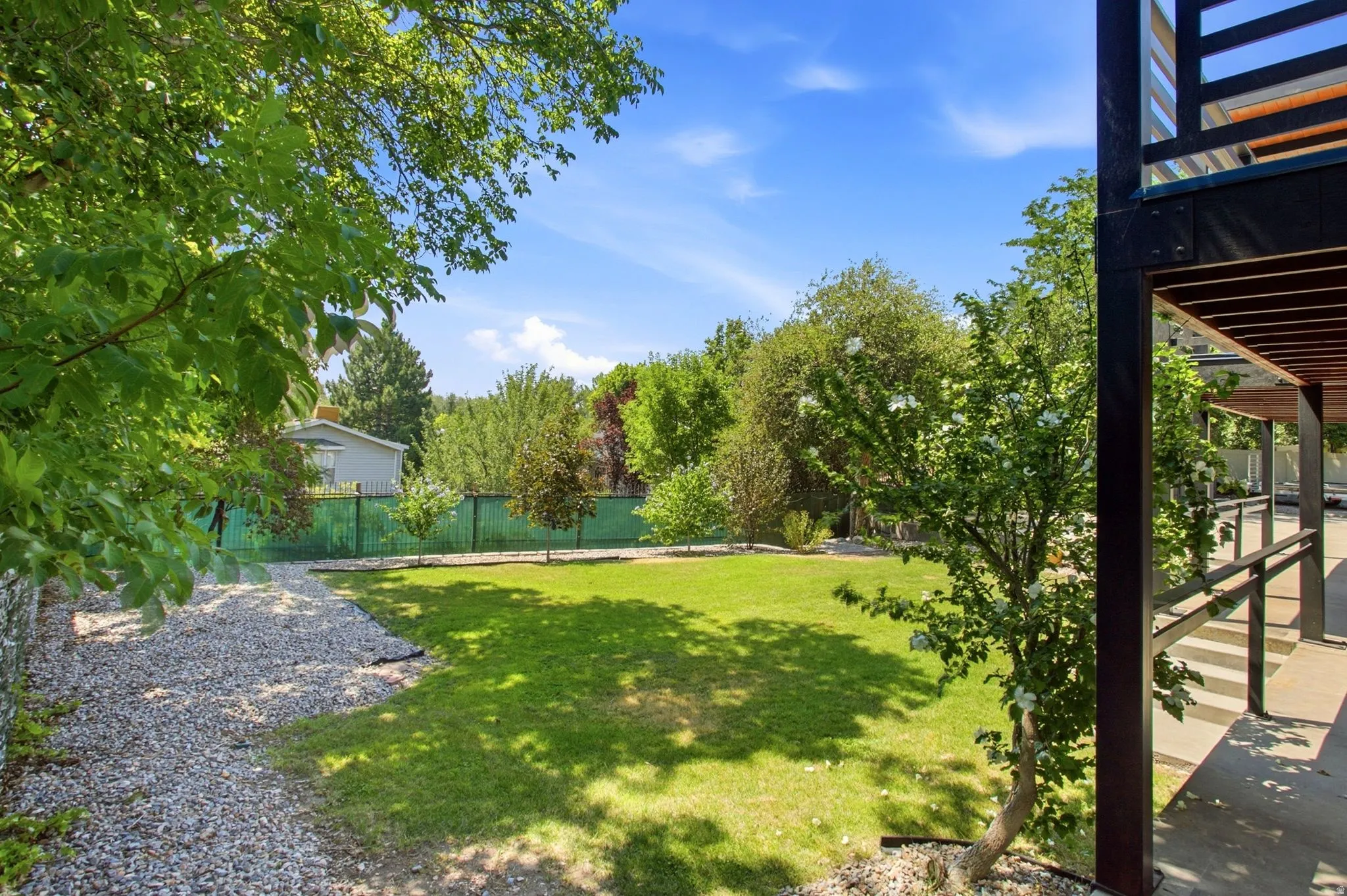 Expansive lawn area, mature trees, gravel pathways, and a covered patio with dark wood accents