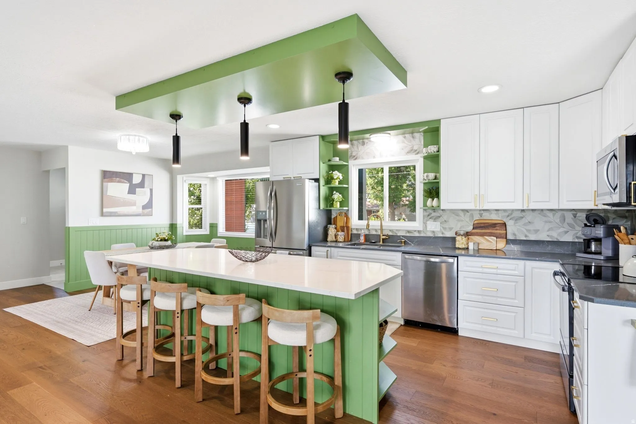 Spacious kitchen with a central island featuring a white countertop, stainless steel appliances, white cabinetry, and hardwood flooring