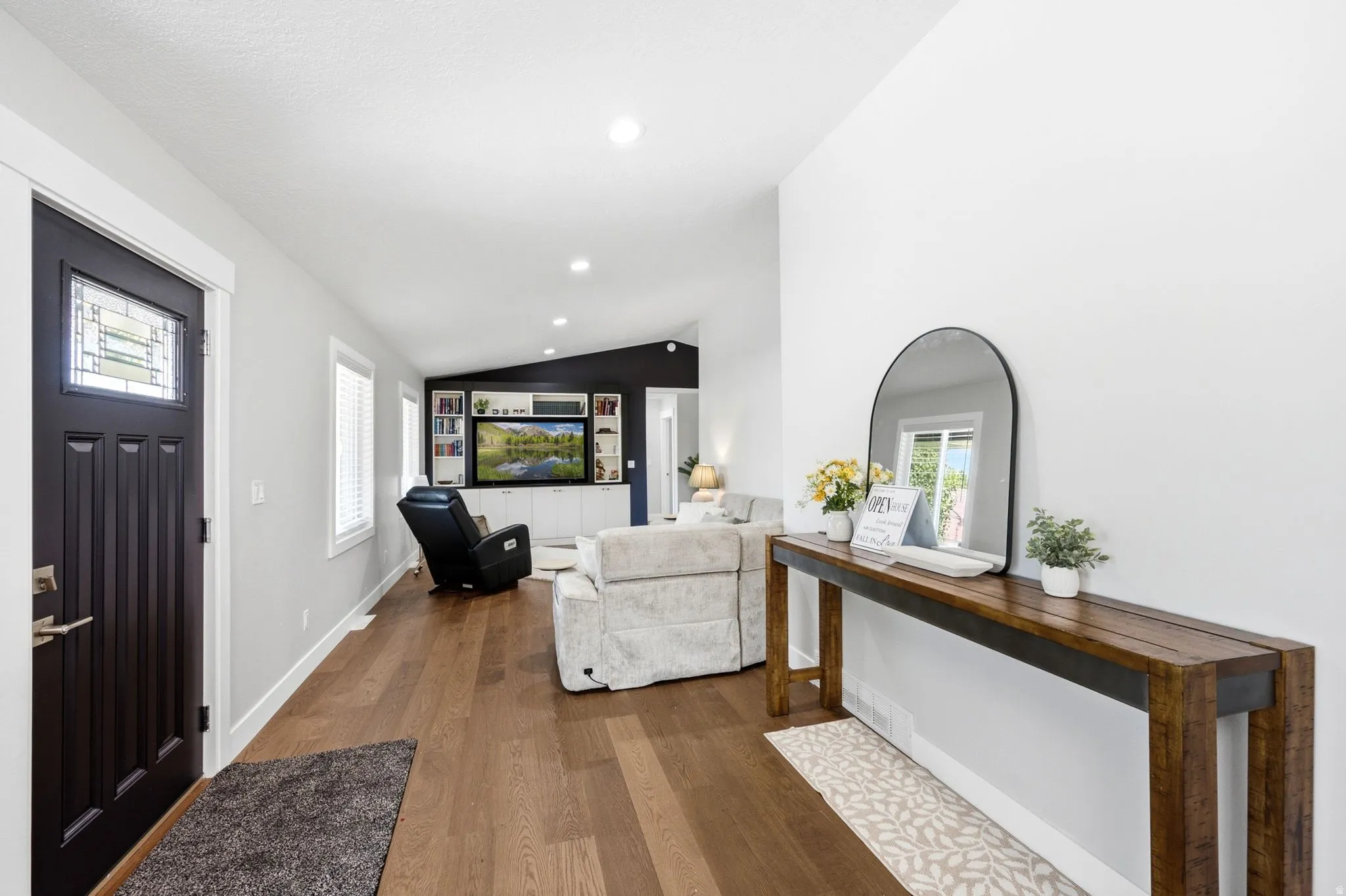 Rich wood-finish flooring, recessed lighting, white trim, custom built-in cabinetry, and a decorative front entry door with leaded glass