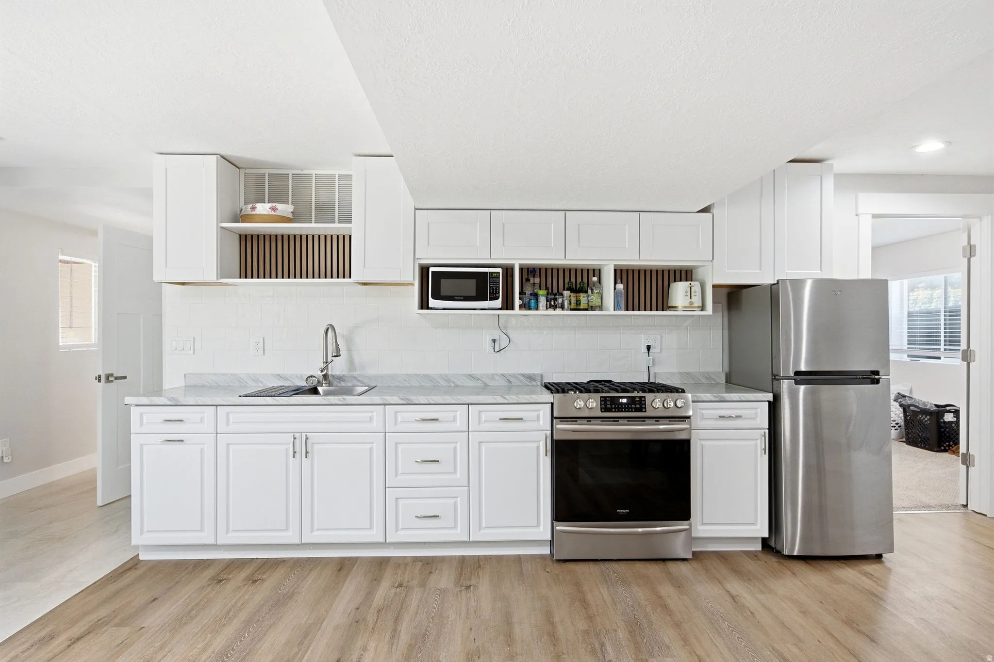 White cabinetry with brushed nickel hardware, stainless steel appliances, marble-finish countertops, subway tile backsplash, and wood-finish flooring