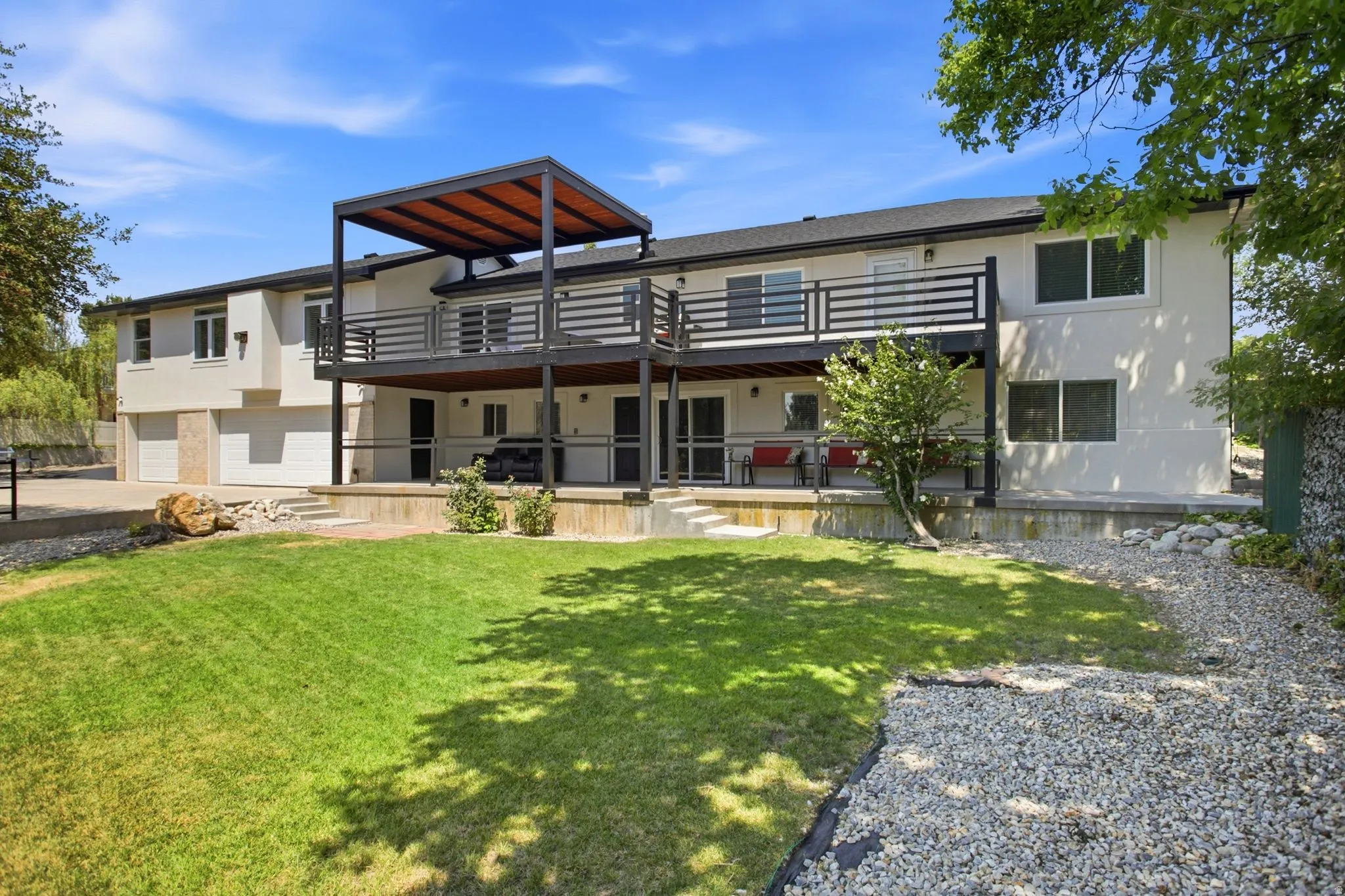 Expansive backyard featuring a manicured lawn, multi-level deck with a pergola, and a lower-level patio