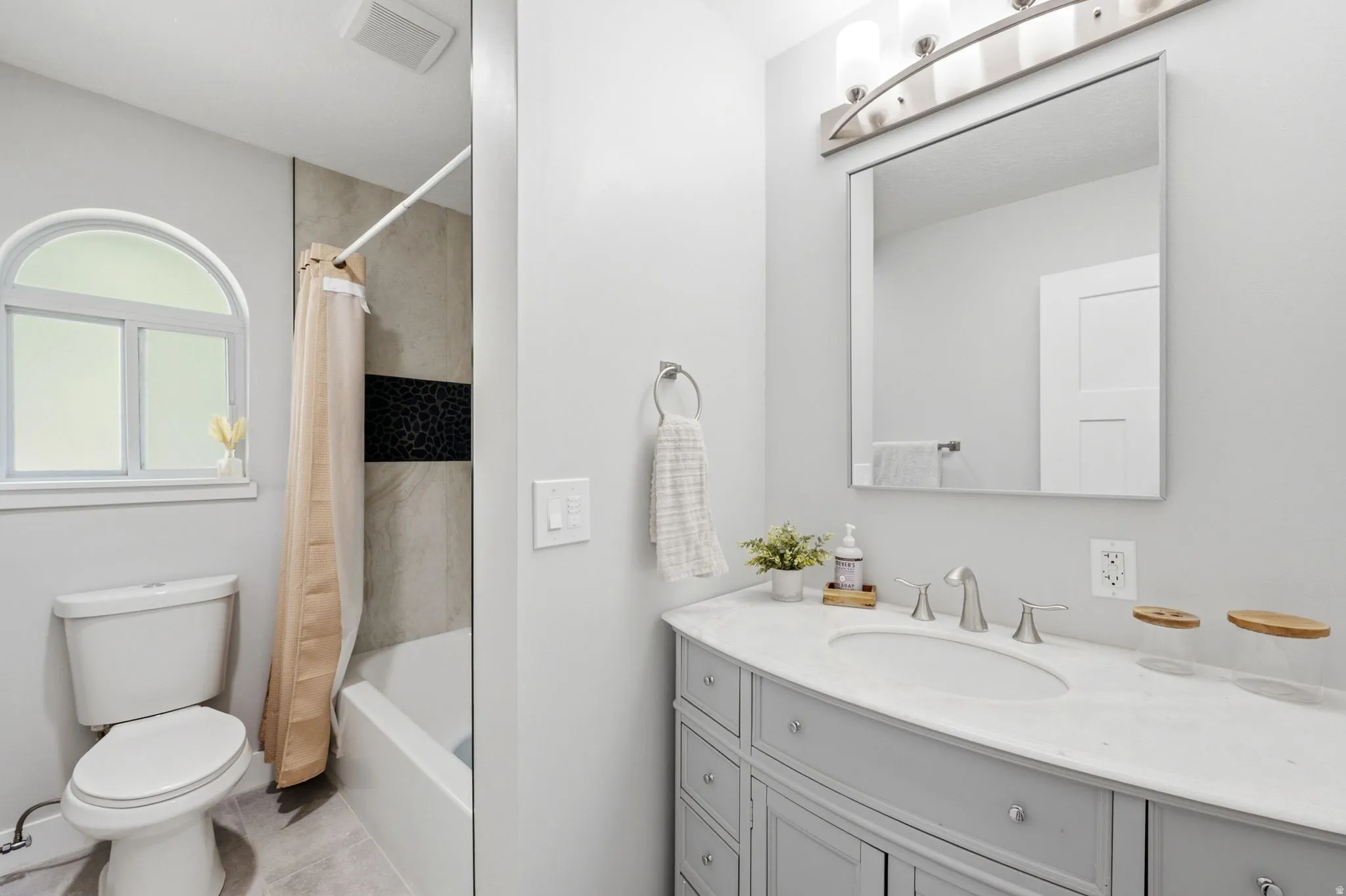 Bathroom featuring a built-in vanity with light gray cabinetry, an undermount sink, a large mirror, and a tiled shower with an arched window