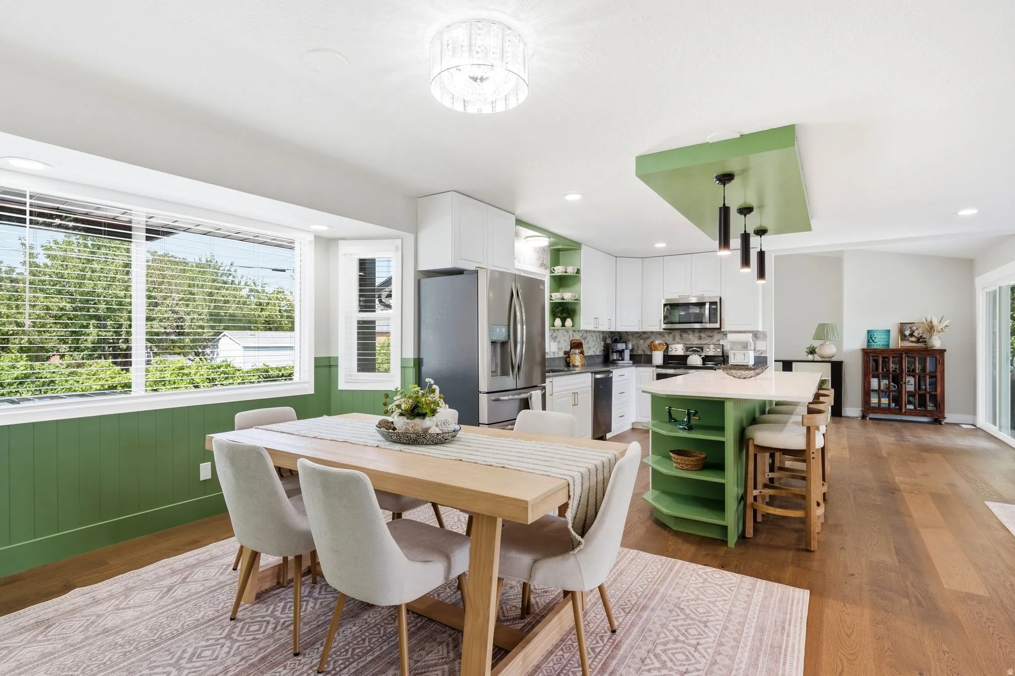 Open-concept living space featuring wood-finish flooring, a contemporary kitchen island with integrated shelving, and white cabinetry
