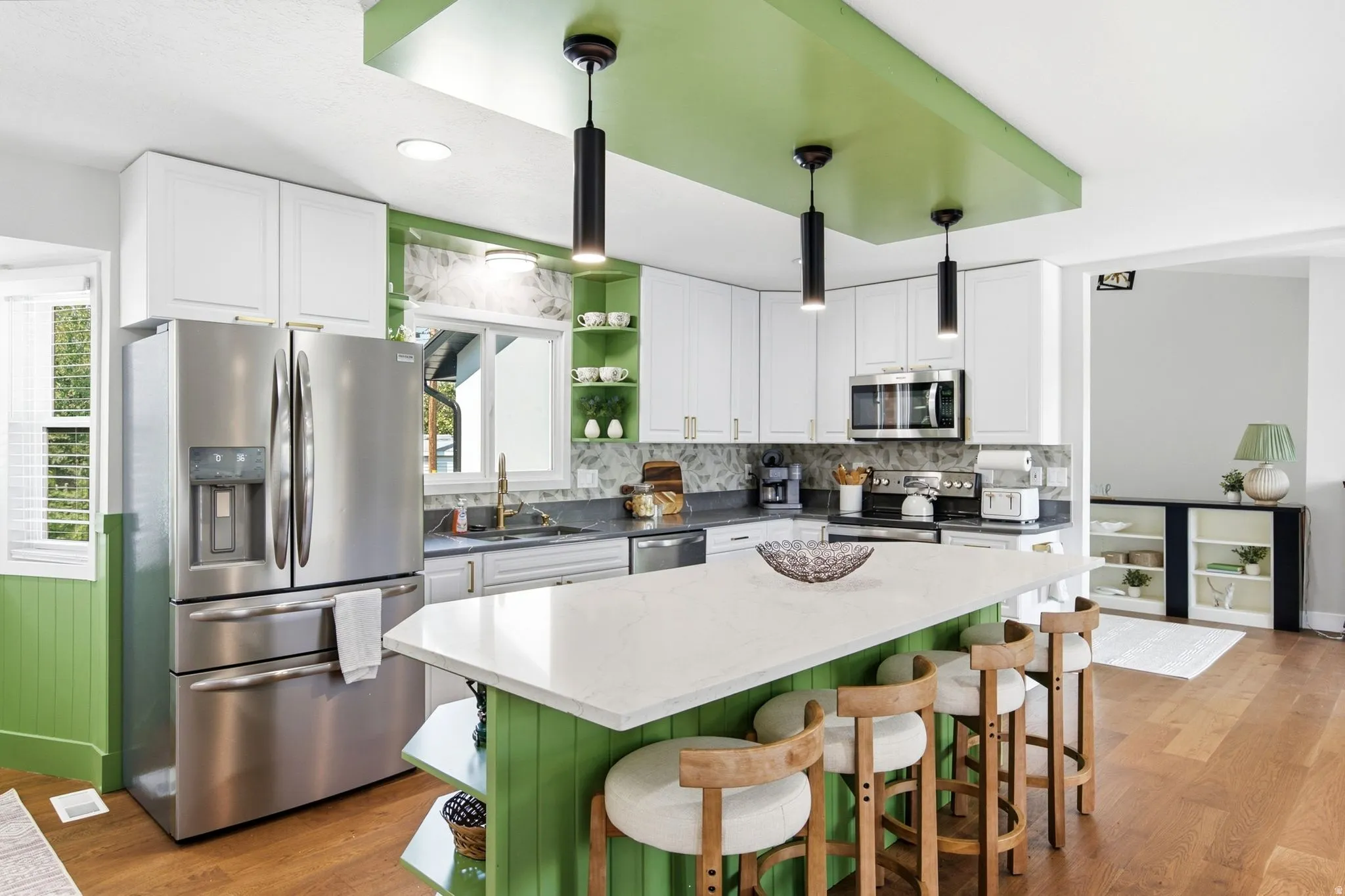 Kitchen featuring stainless steel appliances, white cabinetry, a central island with a light-colored countertop, three pendant lights, and wood-finish flooring