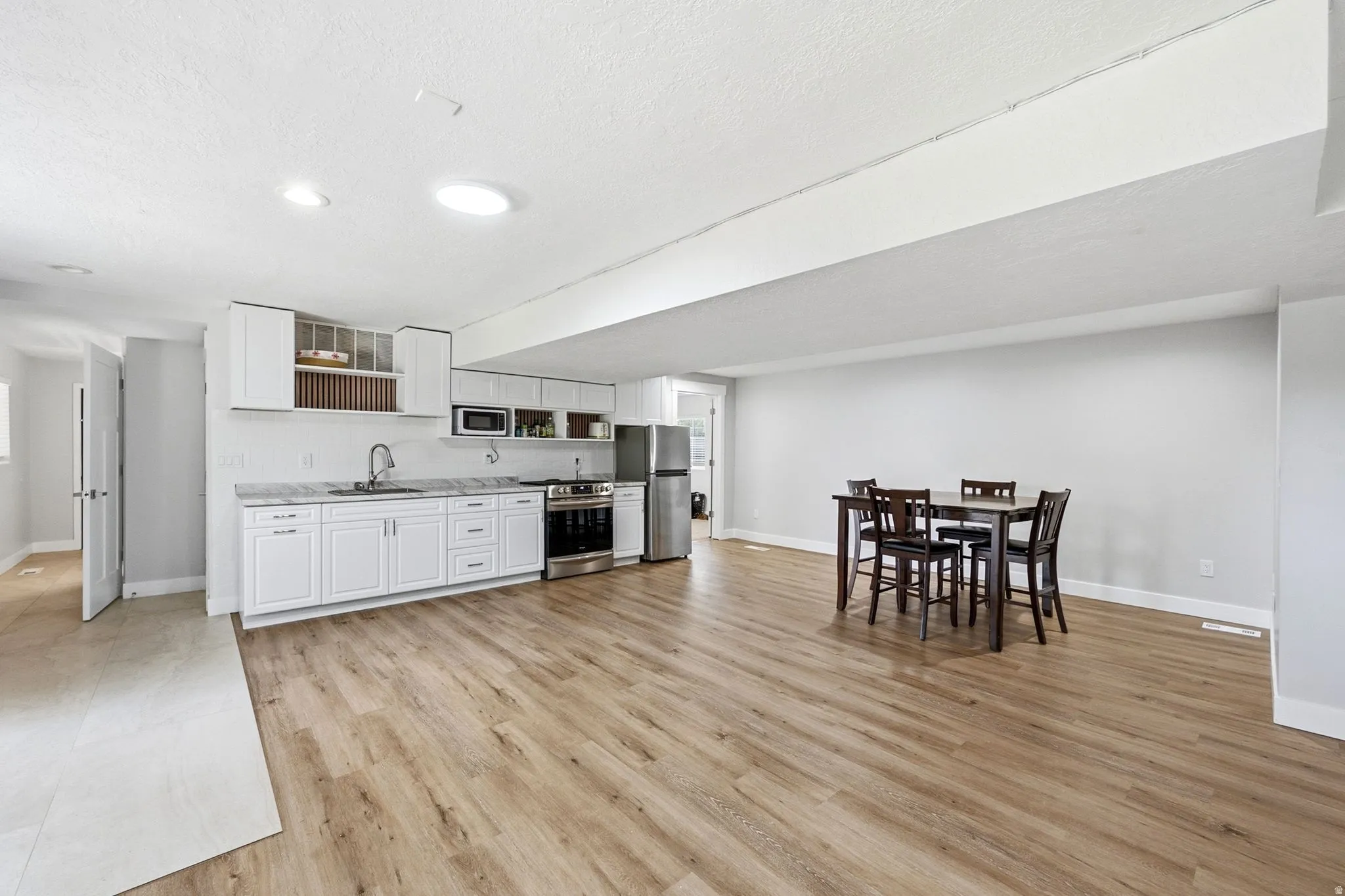 Open-concept room featuring wood-finish flooring, white cabinetry, stainless steel appliances, and recessed lighting
