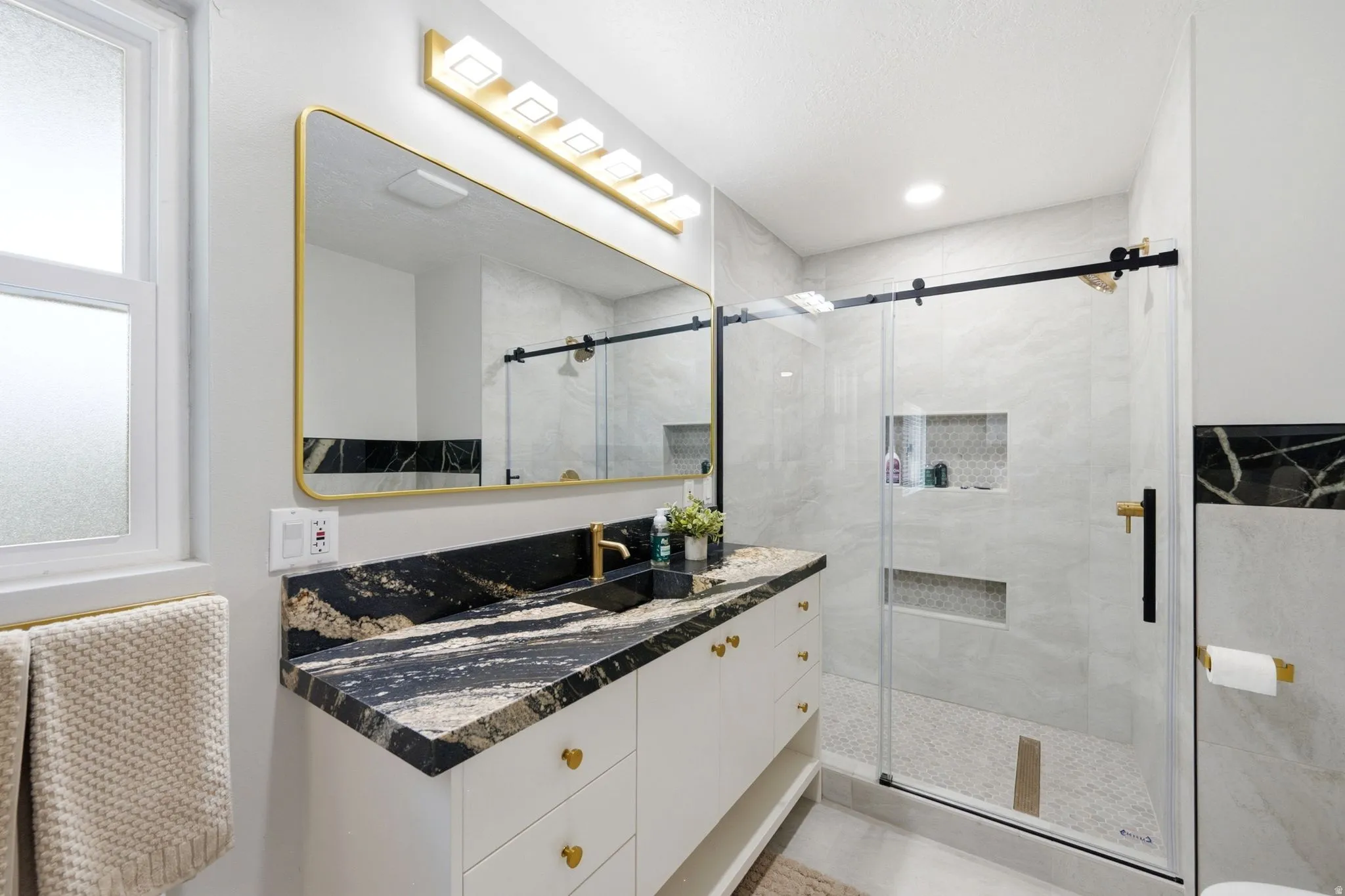 Bathroom featuring a single vanity with a black and gold patterned countertop, a gold-framed mirror, and a gold-finished lighting fixture