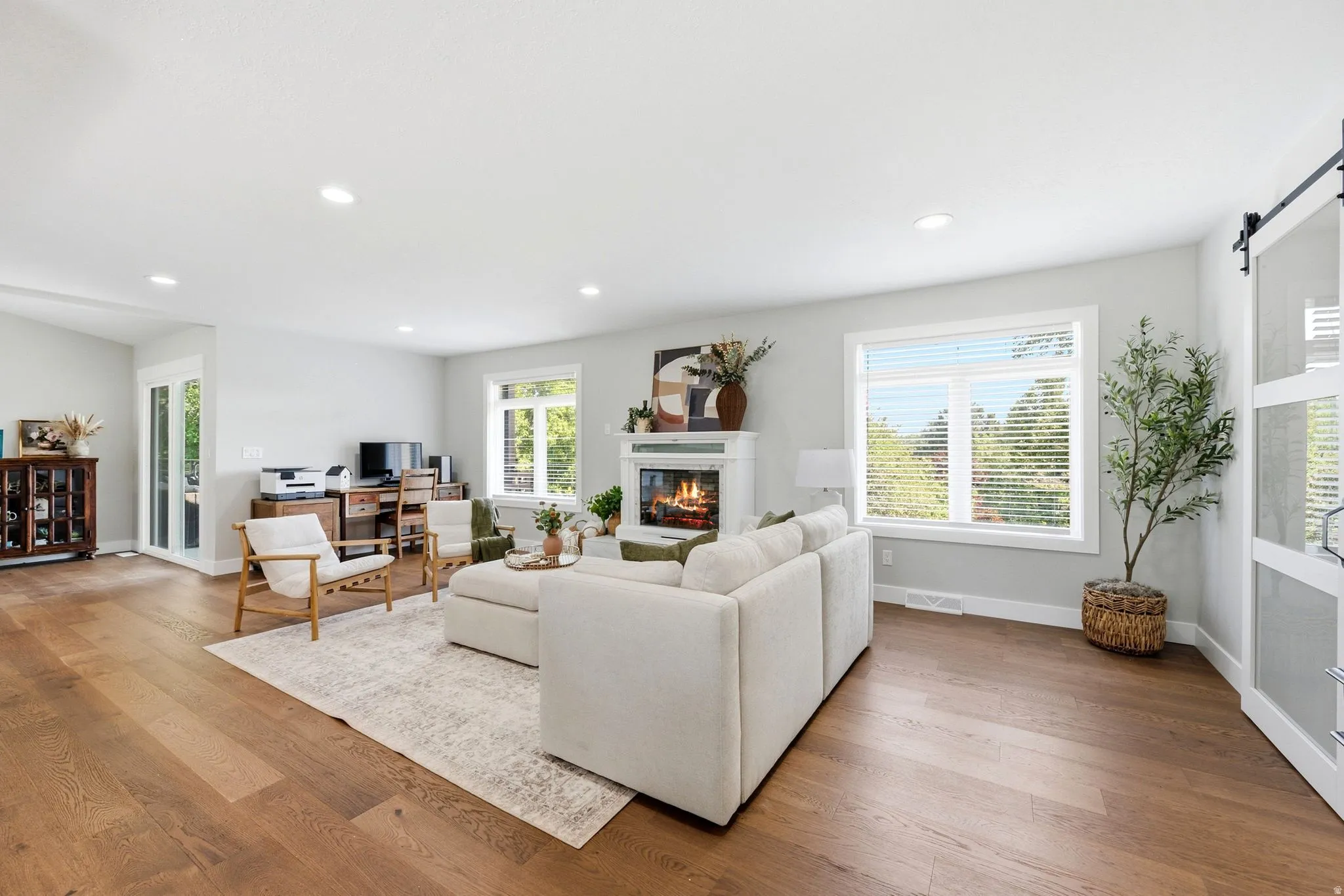 Spacious living area featuring wood-finish flooring, a fireplace with a white mantel, recessed lighting, and large windows