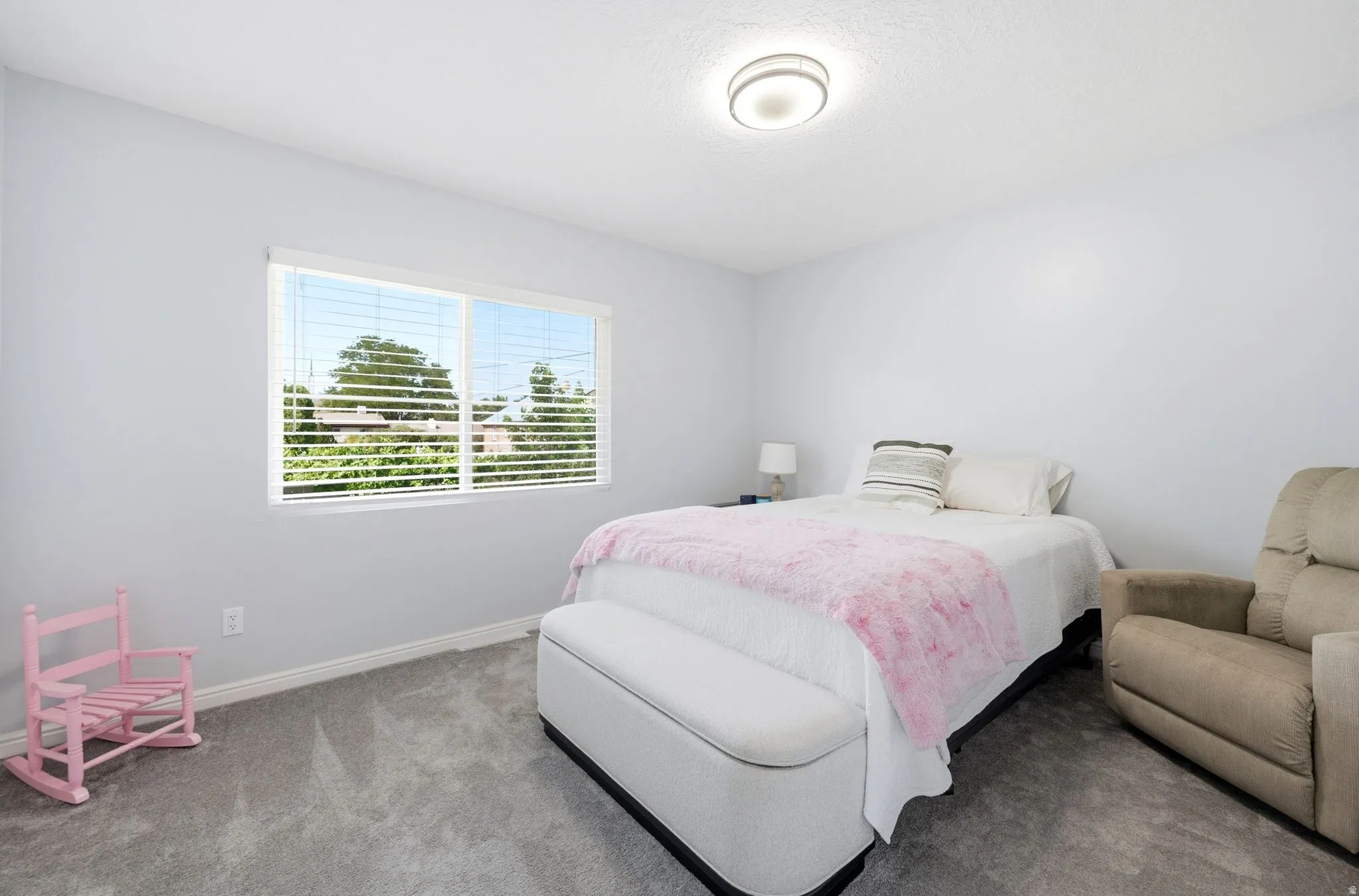 White walls, grey carpet, ceiling-mounted light fixture, and a window with blinds