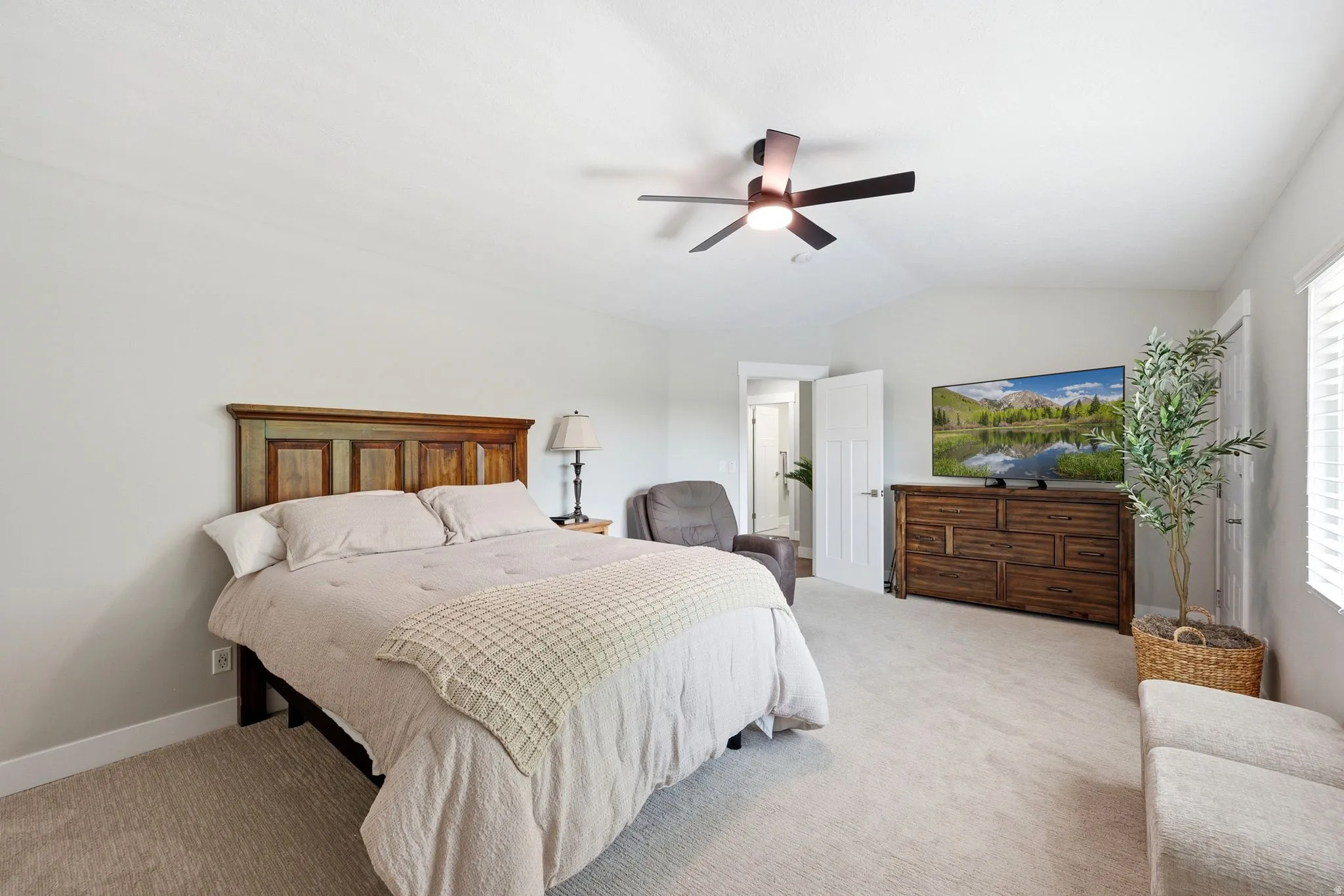 Vaulted ceiling, ceiling fan with integrated lighting, window with blinds, light-toned carpet flooring, white interior doors