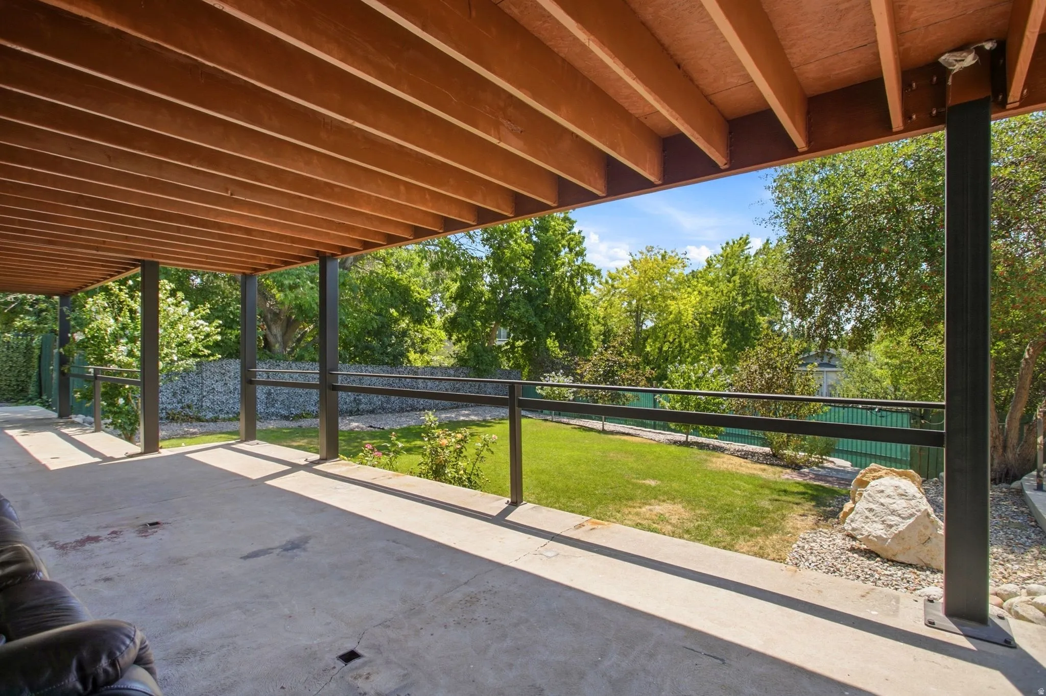 Covered patio with concrete flooring, wood-paneled ceiling, and black support columns