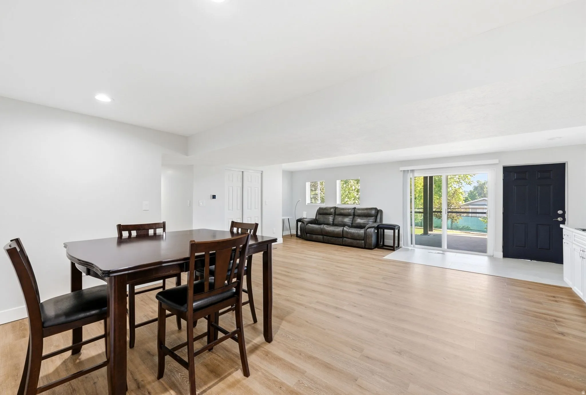 Recessed ceiling lighting, wood-finish flooring, sliding glass patio door, white interior walls, and a dark entry door