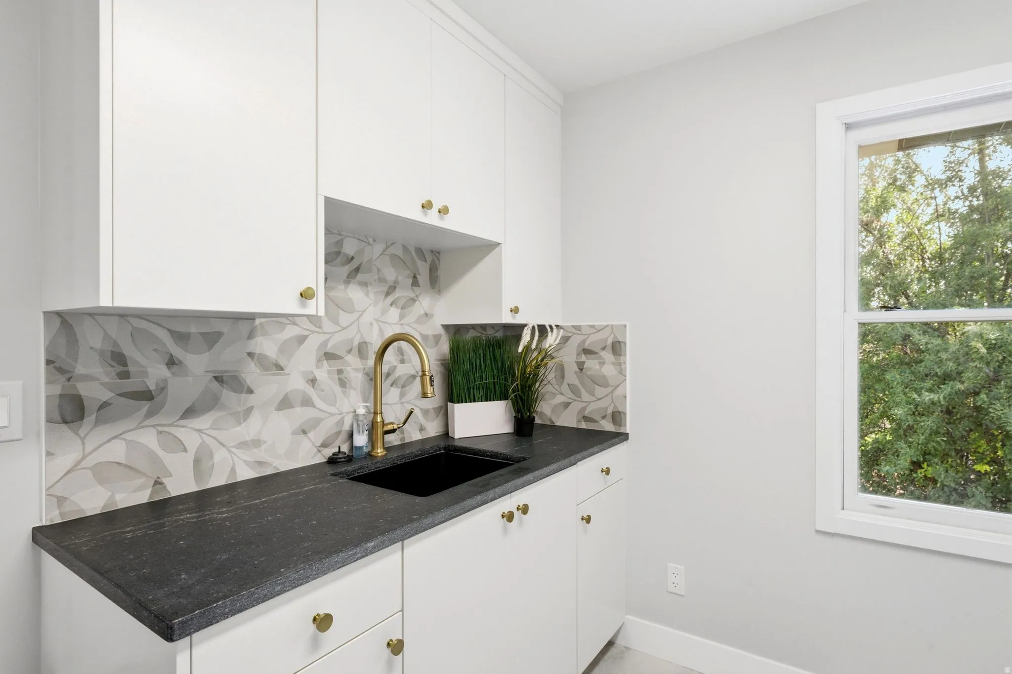 White cabinetry with gold-toned hardware, dark-toned countertop, black undermount sink, and a gold-toned gooseneck faucet
