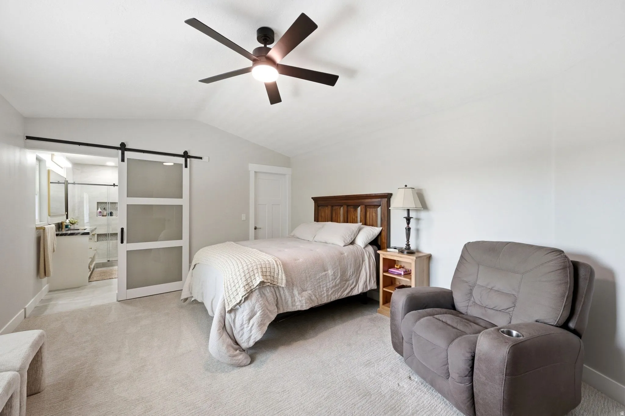 Spacious primary bedroom featuring neutral carpeting, wood-frame bed with headboard, ceiling fan with dark blades, and abundant natural light from multiple windows